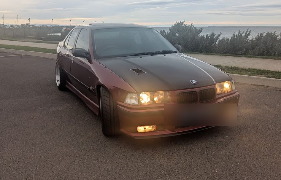 A member's BMW E36 parked by the bay at dusk